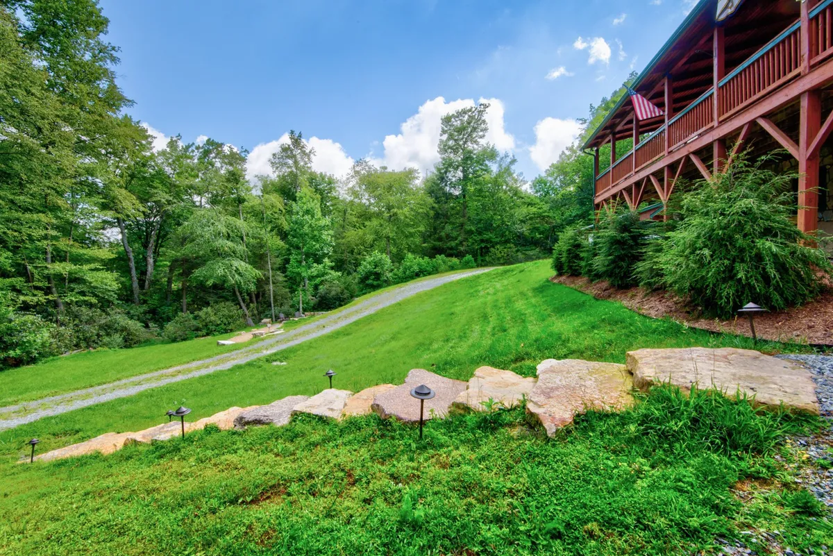 A stone pathway winds through greenery to a deck adorned with an American flag. The lush surroundings and inviting outdoor living space suggest easy access to outdoor activities and relaxing after a day of exploring.