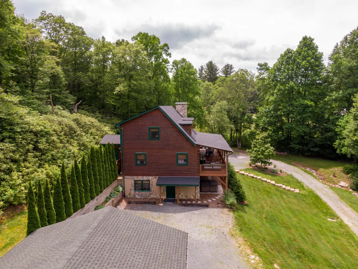 This image features the home's wooden exterior, a spacious deck area, and lush greenery that surrounds the property. The deck provides a natural vantage point for stargazing or morning coffee, emphasizing the outdoor lifestyle and the property's idyllic setting near Blowing Rock’s attractions.