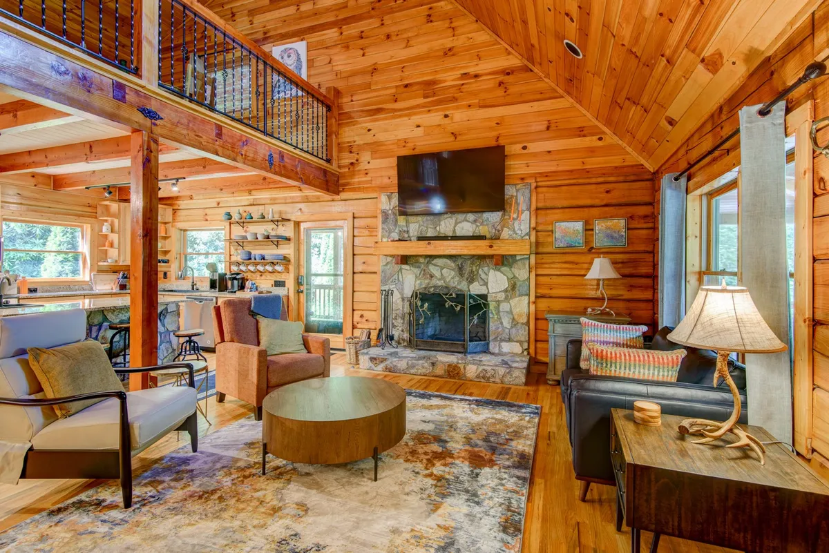 An interior scene reveals a warm, welcoming living area with a fireplace, comfortable sofa seating, and expansive windows framing the views outside. The cozy gathering space is perfect for relaxing with family after a day exploring downtown Blowing Rock or attending seasonal events.