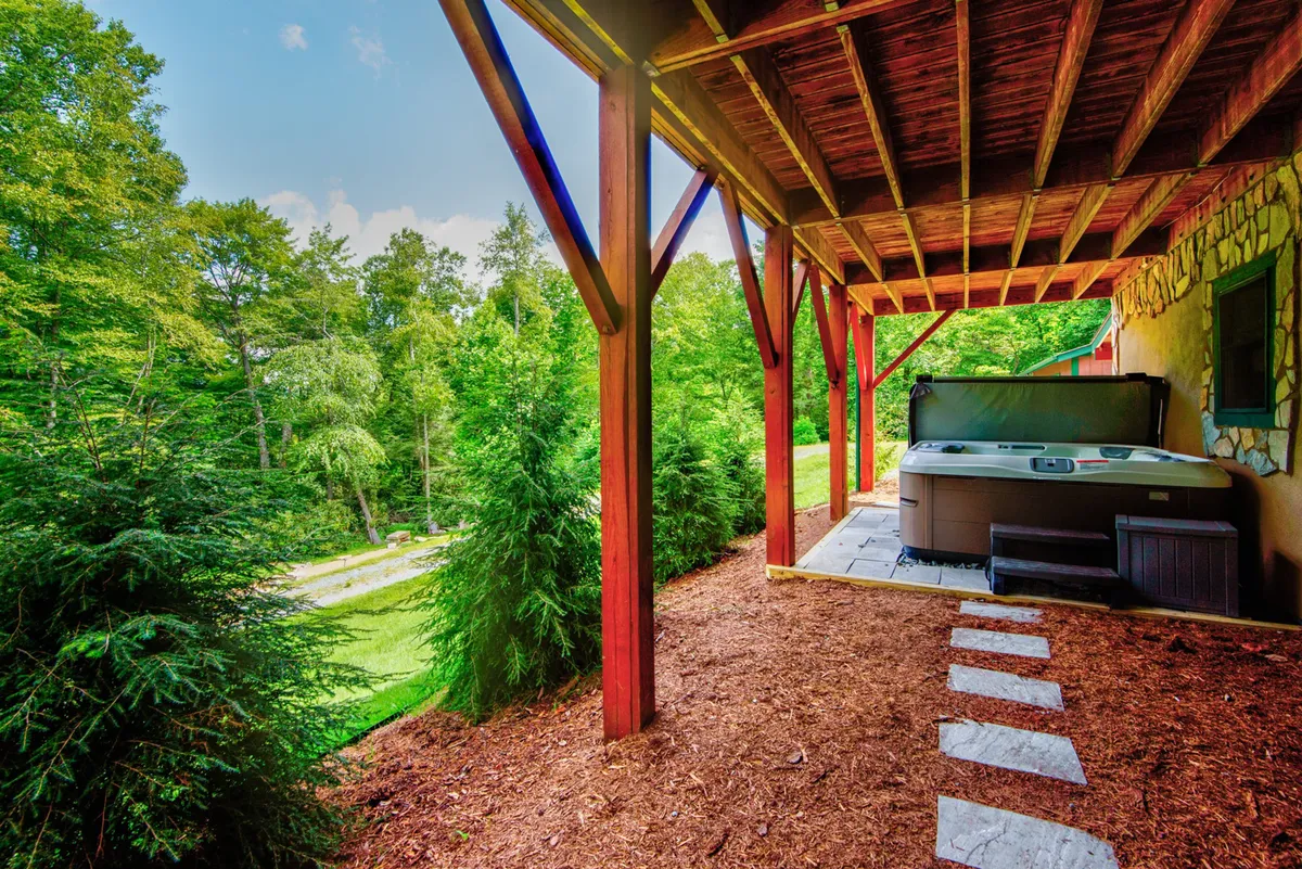 The inviting hot tub sits beneath wooden beams, overlooking vibrant greenery and a stone pathway. The tranquil setting blends relaxation with the outdoors, perfect for soothing muscles after a day of hiking or biking.