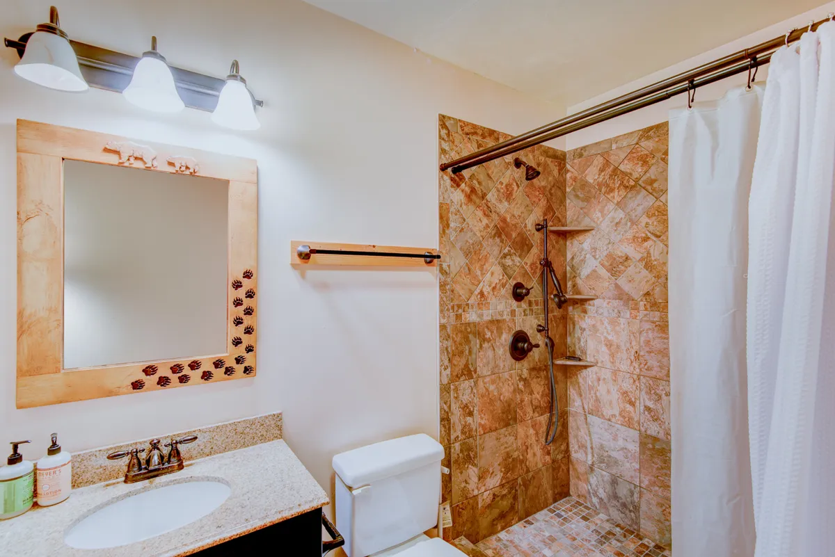 A modern bathroom featuring a large mirror, a walk-in shower with glass doors, a stylish sink, and a calming tiled wall. The space is fresh and spa-like, providing a perfect spot for rejuvenation.