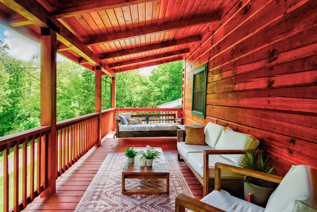 A spacious wooden deck with comfortable seating arrangements, surrounded by lush greenery and a decorative rug that creates a cozy atmosphere for relaxation or entertaining guests. The deck overlooks the natural beauty of the Blue Ridge Mountains, with sunlight filtering through the trees.
