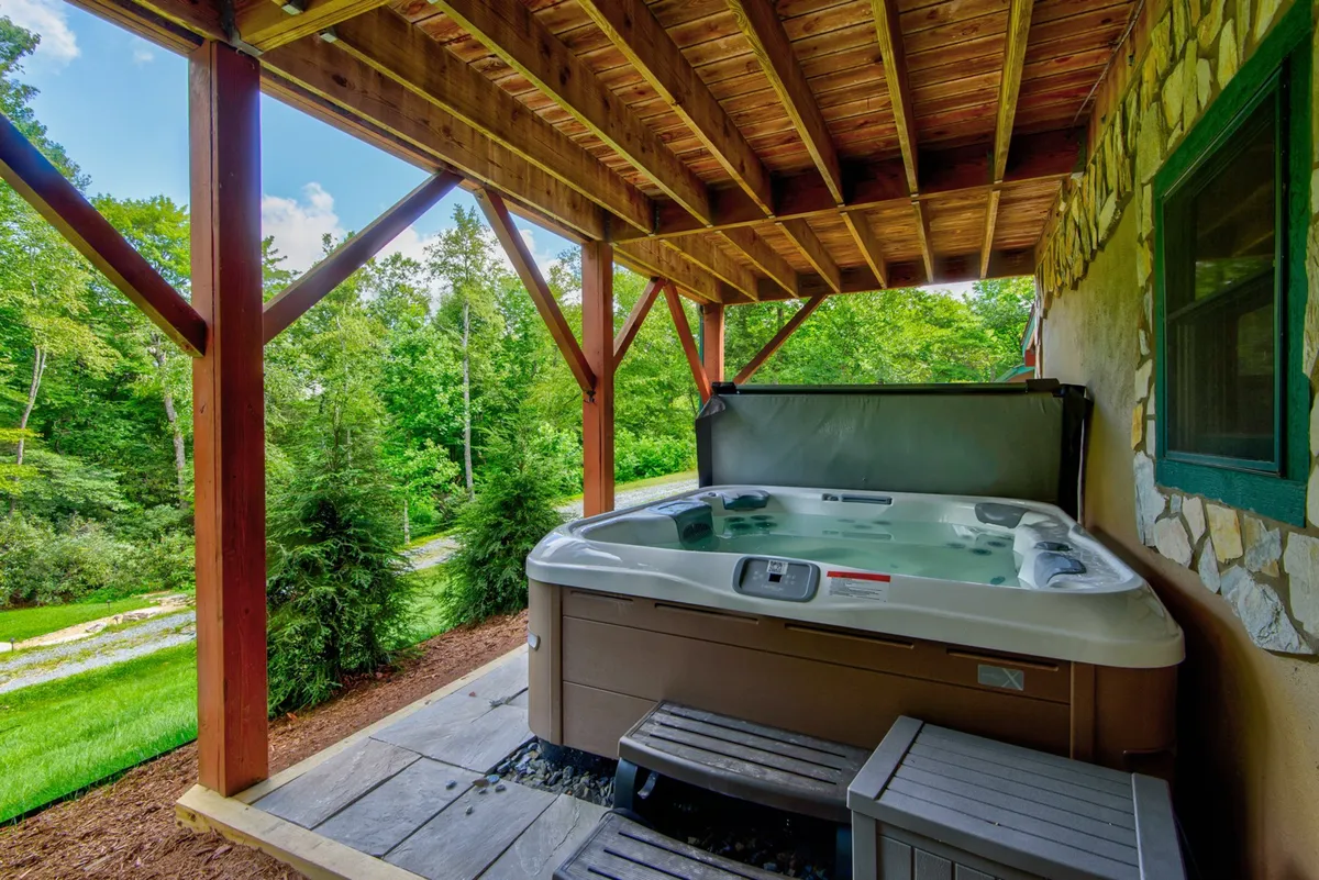 A tranquil hot tub set beneath a wooden structure and surrounded by vibrant greenery. The hot tub is positioned to offer privacy while still allowing guests to immerse themselves in the scenic outdoor environment, ideal for relaxation after a day of adventure.