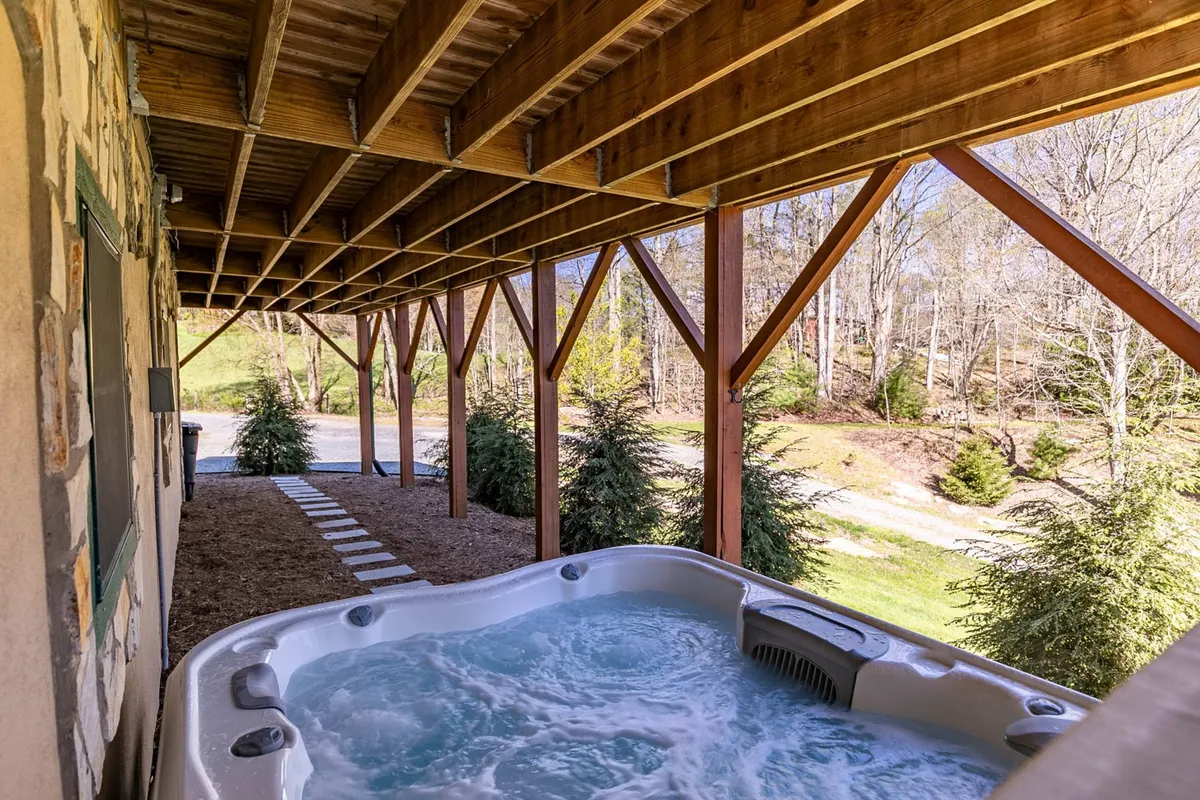 The image highlights an outdoor hot tub sheltered by wooden beams, overlooking the scenic mountain landscape. The natural setting creates an inviting space to unwind under the open sky.