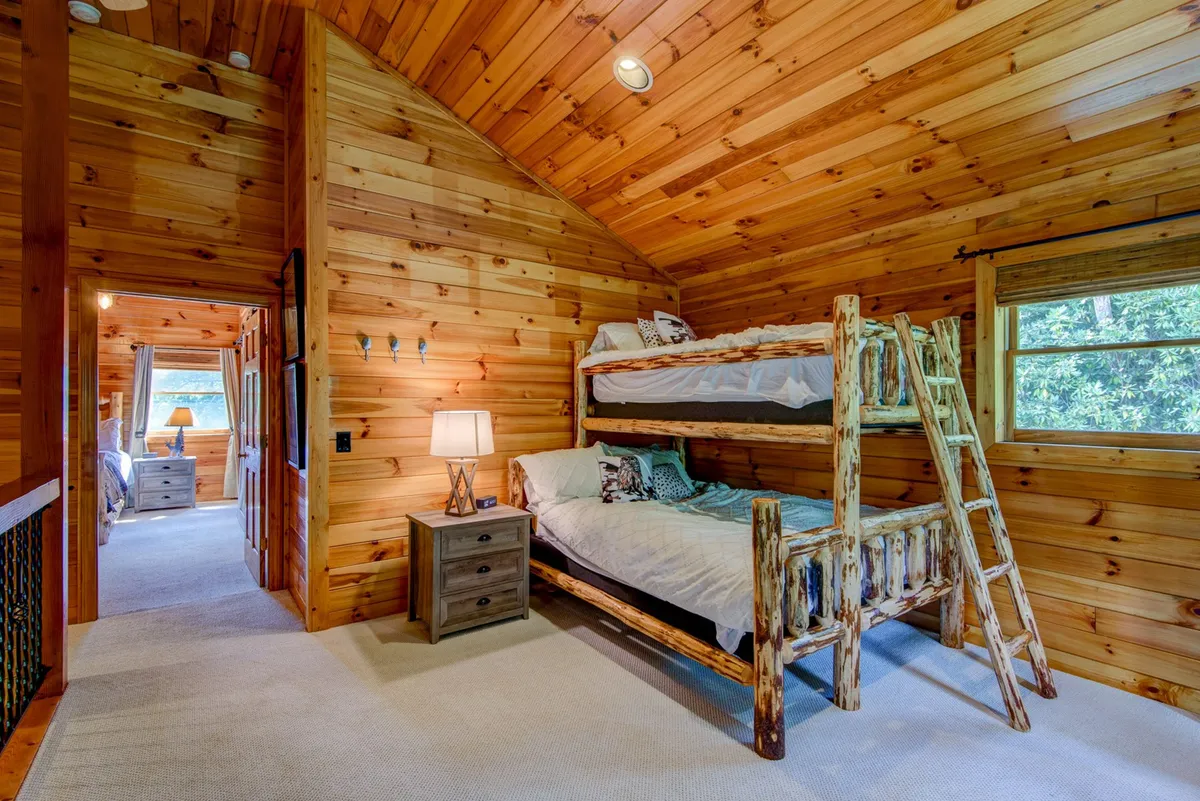 A cheerful, kid-friendly loft featuring a bunk bed, a nightstand with a lamp, and a window with a view. The playful and warm setup hints at a space where kids can play games, read, or enjoy shared laughter during sleepovers.